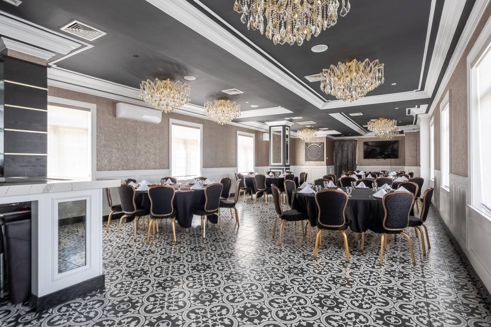 Wide view of The Chandelier Room with crystal chandeliers, patterned tile floor and round tables in black linen