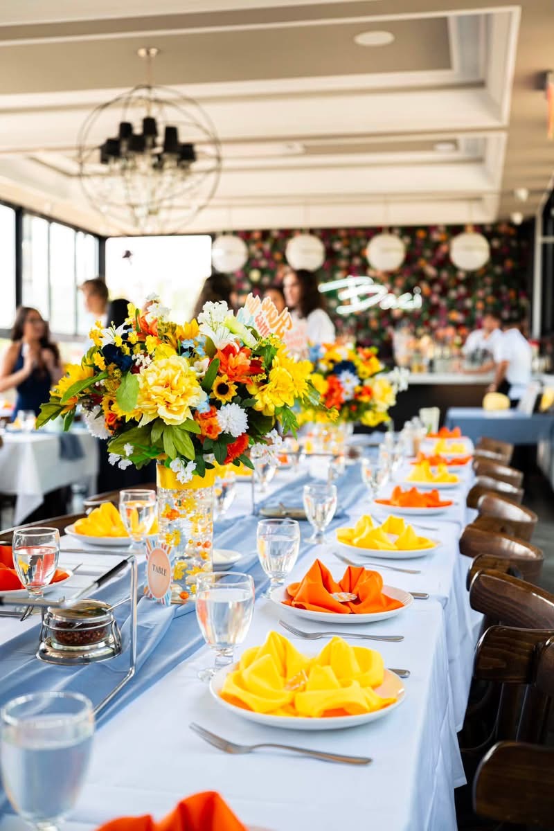 Long banquet table on The Rooftop with vivid floral centerpieces and the Baci flower wall behind